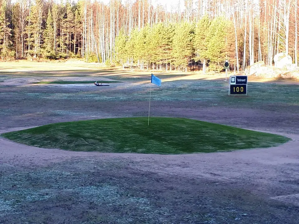 Pyöreä tekonurmikohdeviheriö rangella, lippu ja 100 metrin kyltti.
