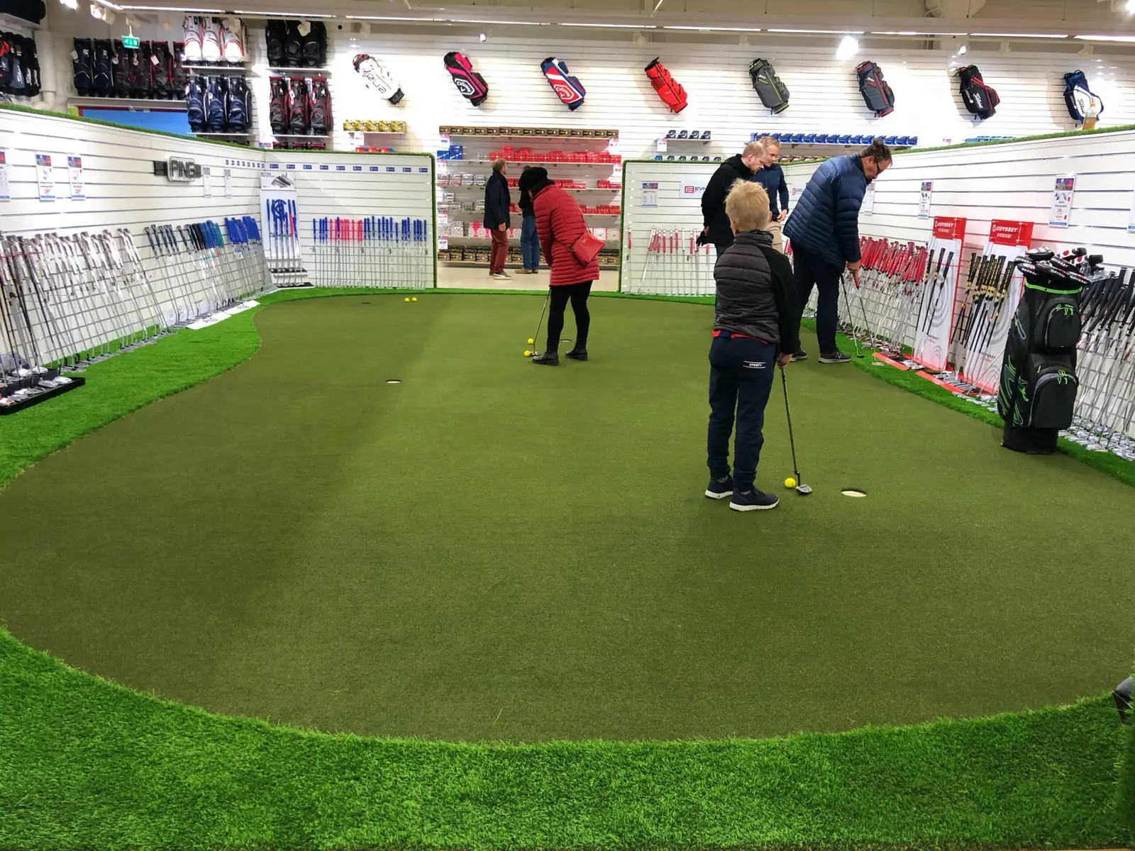 Asiakkaat kokeilevat puttipintaa golfmyymälän puttialueella.