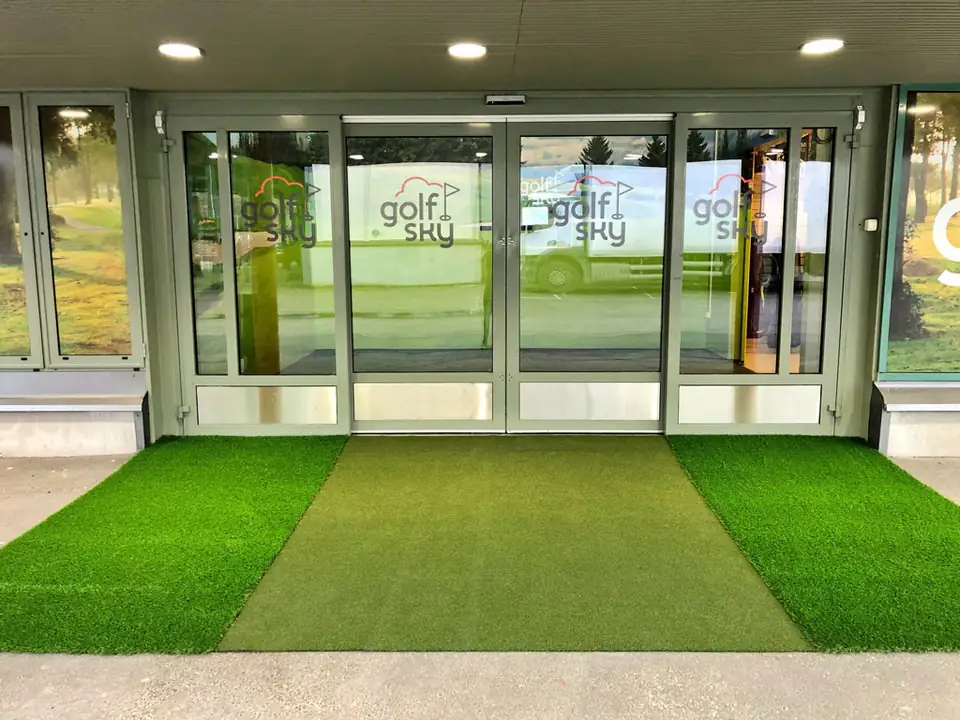 Tekonurmi golfmyymälän sisäänkäynnillä liukuovien edessä.