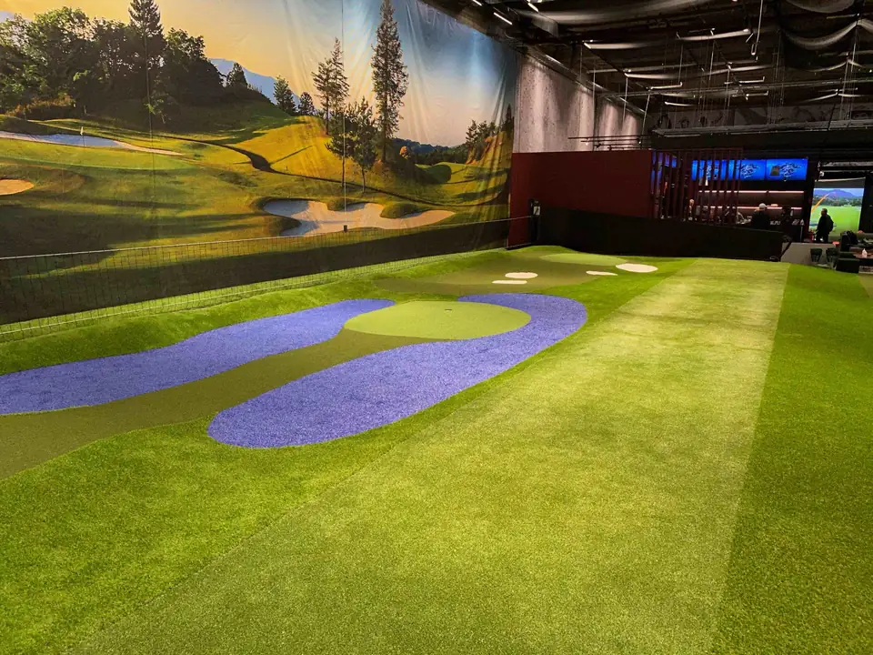 GoGolf Loungen halli: kumpuilevia viheriöitä, sinistä vettä jäljittelevää nurmea ja golfkenttää esittävä seinämaalaus.