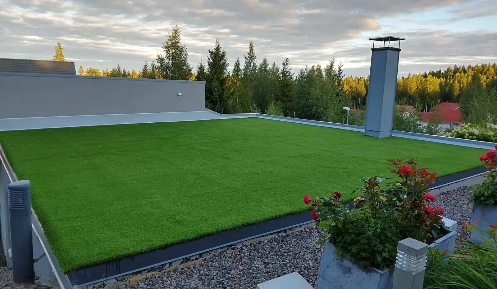 Tekonurmi kattoterassilla, reunalla ruusuja ruukuissa ja taustalla metsää.