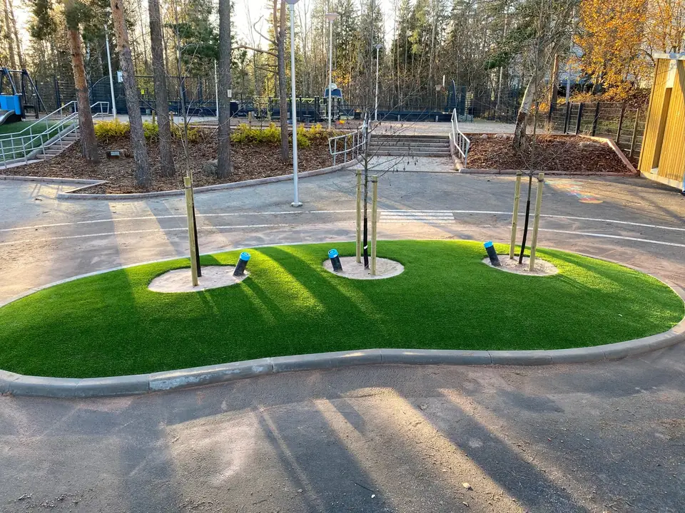 Kaareva tekonurmialue pihan istutusten keskellä.