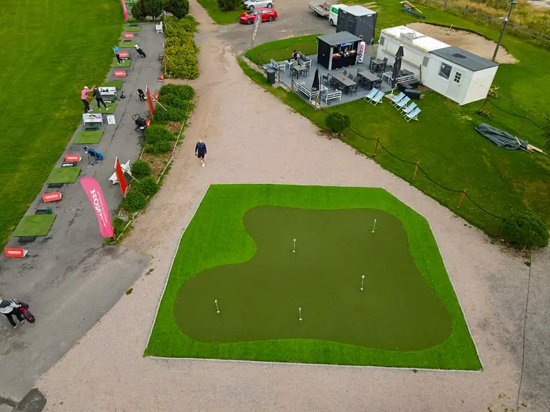 Ilmakuva tekonurmiviheriöstä golfkentän klubirakennuksen vieressä, viheriöllä useita reikiä.